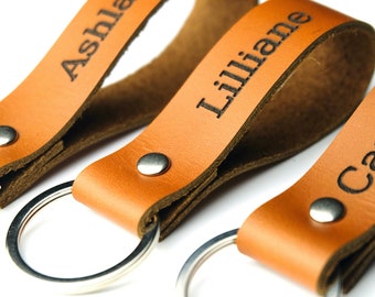 May include: Three brown leather keychains with silver key rings. Each keychain has a name engraved on it: Ashlay, Lilliane, and Carolin.