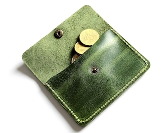 May include: A small green leather coin purse with a flap closure and a snap button. The purse is open and there are a few gold coins inside.
