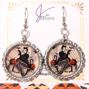 May include: A pair of silver bottle cap earrings with a black cat and pumpkins on a white background. The earrings are silver and have a silver hook.