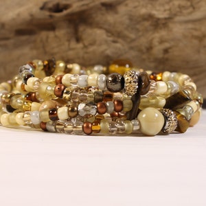 May include: A multi-strand bracelet with brown, gold, and cream colored beads. The bracelet features a variety of bead shapes and sizes, including round, oval, and rectangular beads.