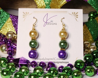 May include: Gold dangle earrings with three beads on each. The beads are purple, green and gold.