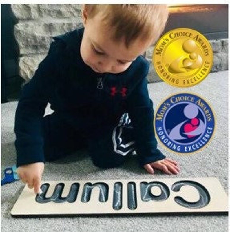 May include: A child is playing with a wooden name puzzle. The puzzle is made of wood and has the name "Callum" spelled out in large letters. The child is using their finger to trace the letters.