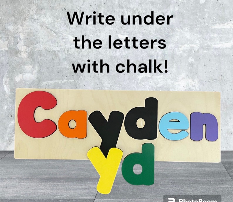 May include: Wooden puzzle with the name Cayden spelled out in colorful letters. The letters are cut out and can be removed. The letters are red, orange, black, light blue, and purple. The background is light wood. The text "Write under the letters with chalk!" is written above the puzzle.