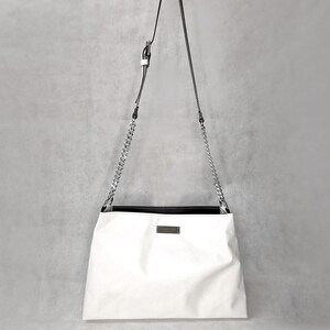 May include: White leather shoulder bag with a silver chain strap and a black leather trim. The bag has a small rectangular label on the front.