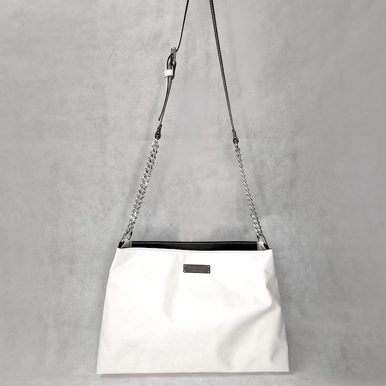 May include: White leather shoulder bag with a silver chain strap and a black leather trim. The bag has a small rectangular label on the front.