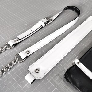 May include: Three white leather straps with silver metal hardware. The straps have stitching along the edges. The straps are on a gray surface.