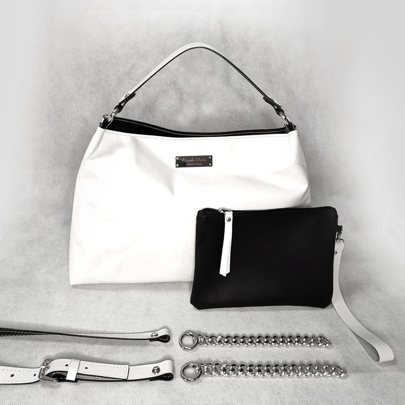 May include: A white leather tote bag with a black leather pocket and a silver chain strap. The bag has a silver logo that says "Angela Davis" on the front.