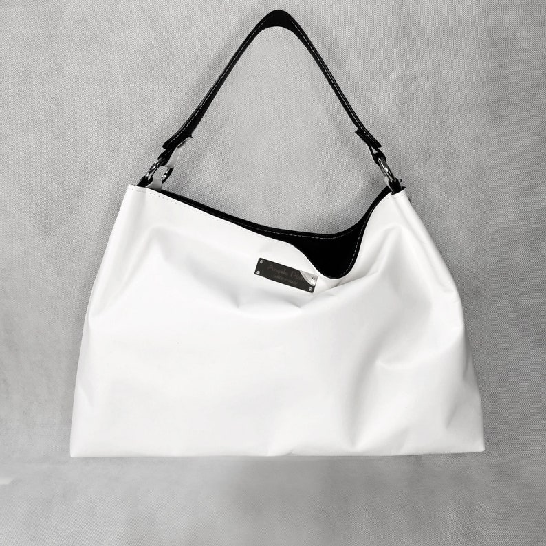 May include: White leather handbag with a black leather trim and a silver metal logo plate.