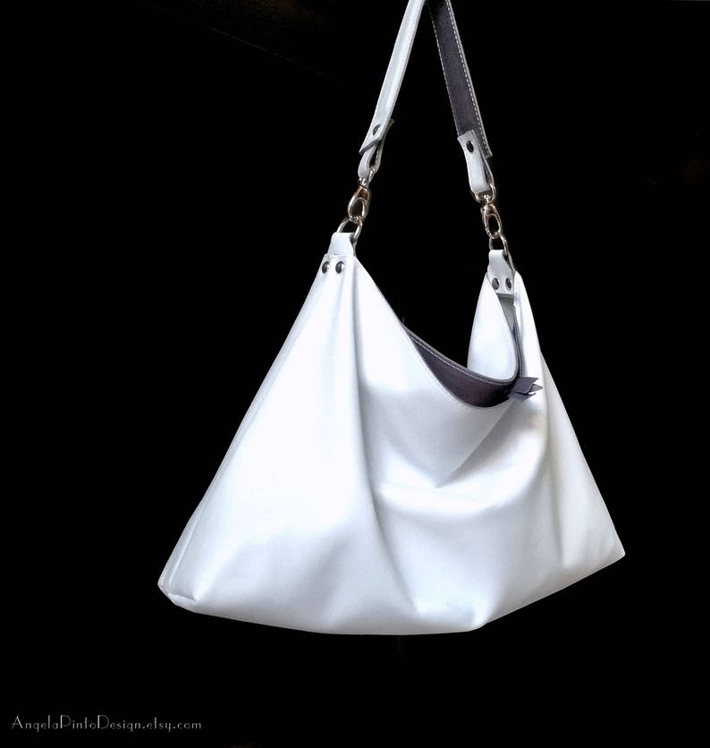 May include: A white leather tote bag with a gray leather strap and silver hardware. The bag has a slouchy, casual look.