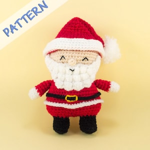 Pode incluir: Um boneco de Papai Noel de croch&ecirc; com um traje vermelho, barba branca e botas pretas. O boneco tem uma borda branca ao redor do chap&eacute;u e um cinto preto com uma fivela dourada.