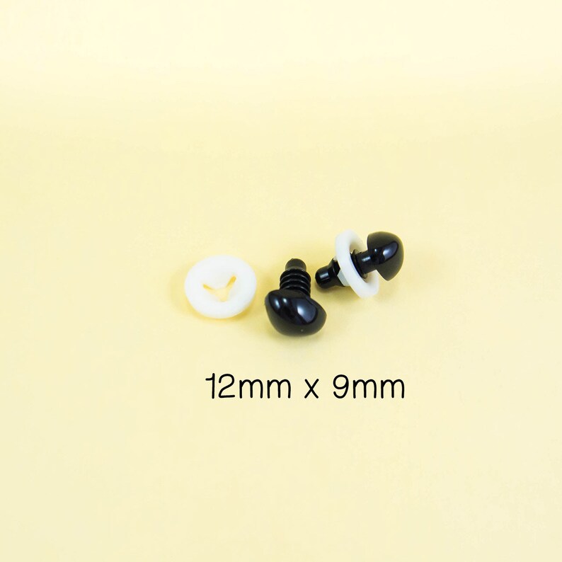 Może przedstawiać: Dwa czarne plastikowe oczy bezpieczeństwa z białymi plastikowymi podkładkami, o wymiarach 12 mm x 9 mm.