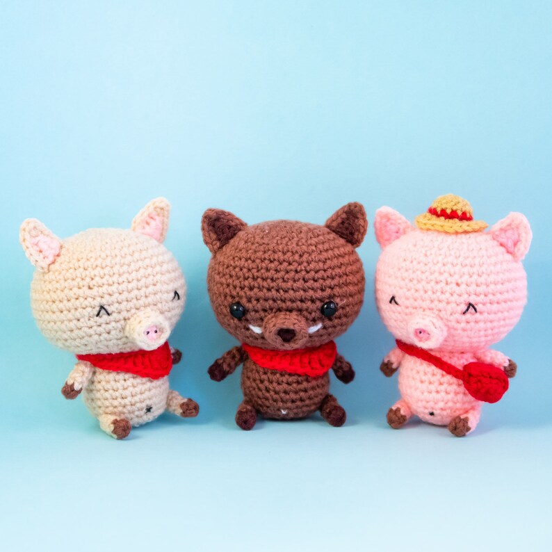 May include: Three crocheted stuffed animals: a brown wolf, a pink pig wearing a straw hat, and a beige pig. All three animals are wearing red scarves.