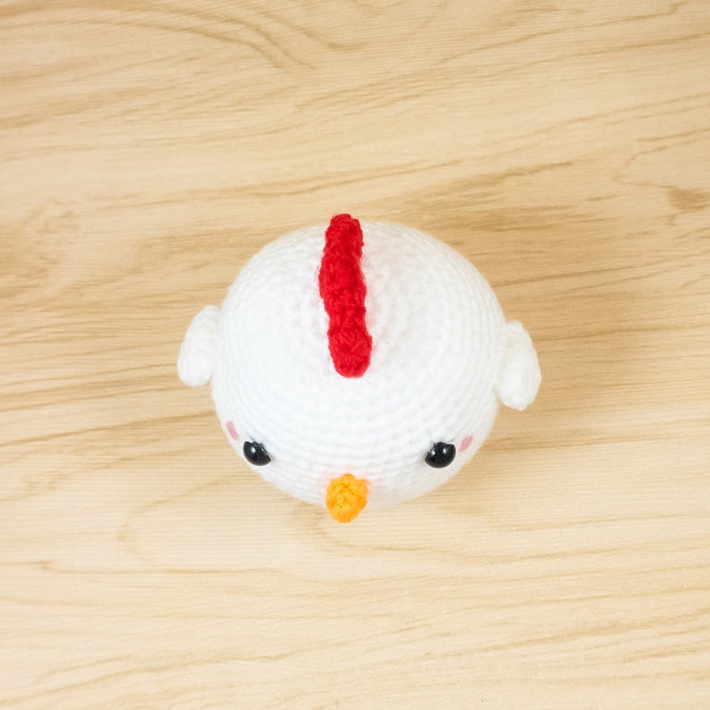 K&ouml;nnte beinhalten: Wei&szlig;es H&auml;kelspielzeug Huhn mit rotem Kamm, schwarzen Augen und orangefarbenem Schnabel.