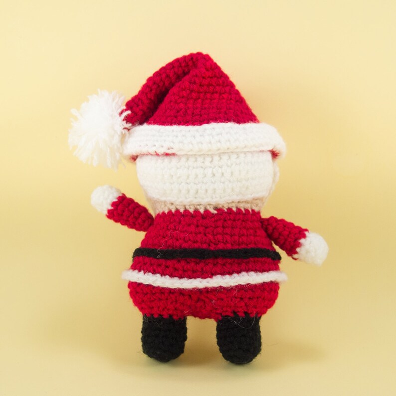 Pode incluir: Um boneco de croch&ecirc; do Papai Noel com um chap&eacute;u vermelho e branco, um terno vermelho e branco e botas pretas.