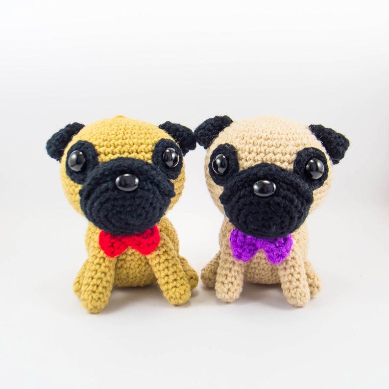 May include: Two crocheted pug dog toys, one is tan with a red bow tie and the other is beige with a purple bow tie.