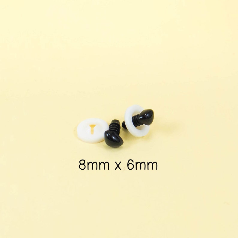 Może przedstawiać: Dwa czarne plastikowe oczy bezpieczeństwa z białymi plastikowymi podkładkami. Oczy mają średnicę 8 mm i wysokość 6 mm. 8 mm x 6 mm