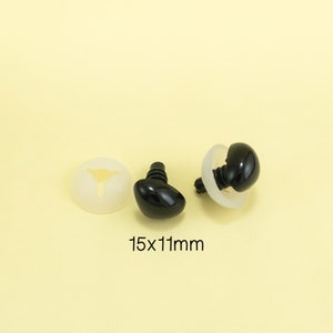 Może przedstawiać: Dwa czarne plastikowe oczy bezpieczeństwa z białymi plastikowymi podkładkami. Oczy mają rozmiar 15 mm x 11 mm.