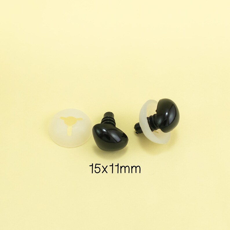 Może przedstawiać: Dwa czarne plastikowe oczy bezpieczeństwa z białymi plastikowymi podkładkami. Oczy mają rozmiar 15 mm x 11 mm.