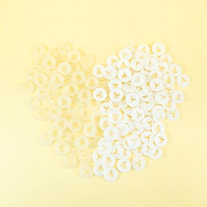 May include: A heart shape made of white plastic fasteners. The fasteners are arranged in a heart shape on a light yellow background.
