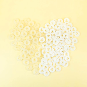 May include: A heart shape made of white plastic fasteners. The fasteners are arranged in a heart shape on a light yellow background.