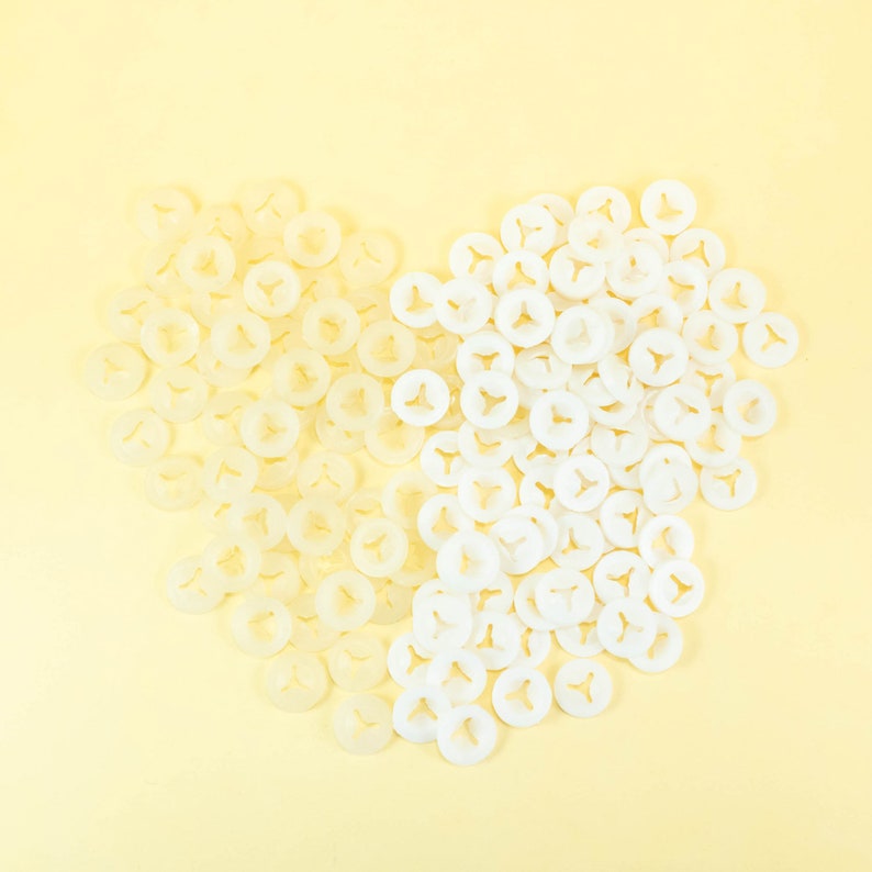 May include: A heart shape made of white plastic fasteners. The fasteners are arranged in a heart shape on a light yellow background.