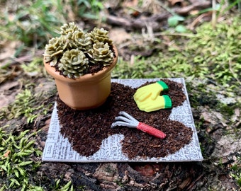 May include: A miniature gardening set with a small terracotta pot filled with green succulents, a pair of yellow gardening gloves, and a small red and silver gardening tool on a piece of brown paper with the word "Headline" printed on it.
