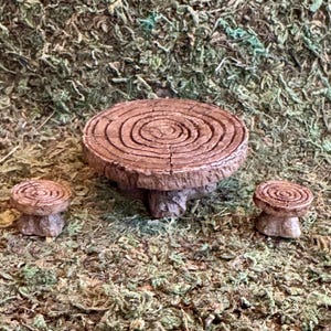 May include: A miniature brown table and two matching stools, each designed to resemble a cross-section of a tree trunk. The surfaces feature detailed concentric rings and textured bark edges, mimicking the appearance of natural wood grain.