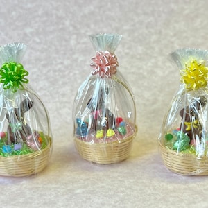 May include: Three small wicker baskets filled with chocolate Easter bunnies and colorful candy eggs. Each basket is wrapped in clear cellophane with a colorful bow.