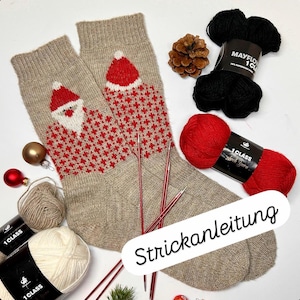 May include: A pair of beige Christmas socks with a Santa Claus design in red and white. Knitting needles, red and black yarn, and white and beige yarn are arranged around the socks. A pine cone and ornaments are also present.