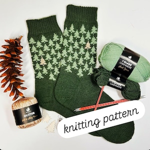 Può includere: Un paio di calzini verdi lavorati a maglia con un motivo ad albero verde chiaro, accanto a filato verde, ferri da maglia e un gomitolo di filato glitterato. Il testo "knitting pattern" è visibile.