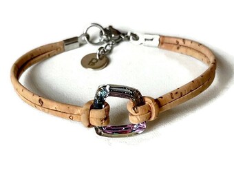 Puede incluir: Pulsera con banda de corcho marrón claro, cierre plateado y pieza central cuadrada iridiscente. La pulsera tiene un pequeño dije redondo con la letra "B". La pulsera está diseñada para el uso diario.