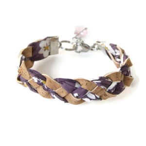 Puede incluir: Un brazalete trenzado hecho de corcho y tela morada con un patr&oacute;n floral blanco. El brazalete tiene un cierre plateado y un dije rosa.
