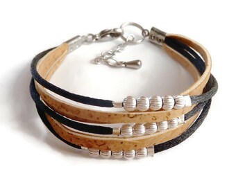 Puede incluir: Un brazalete de múltiples hebras hecho con corcho y cordón negro. El brazalete tiene cuentas plateadas y un cierre de mosquetón.