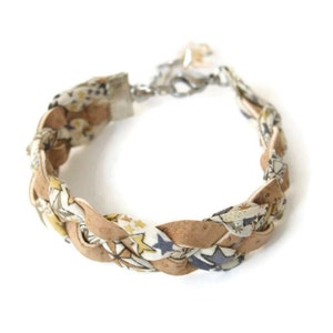 Puede incluir: Un brazalete trenzado hecho de corcho y tela con un fondo blanco y un patr&oacute;n de estrellas azules y flores amarillas. El brazalete tiene un cierre plateado.