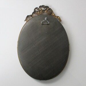May include: Oval-shaped mirror with a gold-colored ornate frame. The frame features a decorative ribbon design.