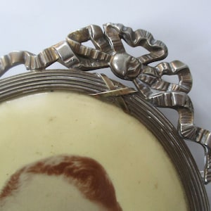 May include: A silver oval picture frame with a decorative bow design. The frame has a raised edge and a smooth, polished finish.