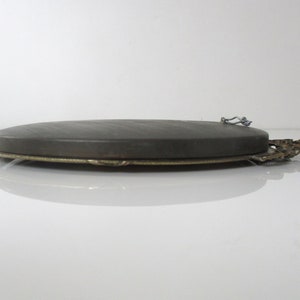 May include: Oval-shaped picture frame with a dark gray backing and a gold-colored metal frame. The frame has a decorative design on the bottom edge and a metal hook on the back for hanging.