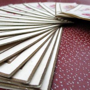 May include: A stack of white cards with brown borders, fanned out in a radial pattern. The cards are arranged in a fan shape, with the top card being the most visible. The cards are all the same size and shape, and they have a simple, elegant design.