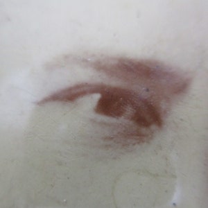 May include: Close-up of a brown eye painted on a white surface. The eye is partially obscured by a white haze.