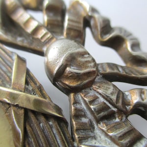 May include: A close-up of a decorative metal ornament featuring a stylized bow with intricate details. The ornament is made of brass and has a worn, antique finish.