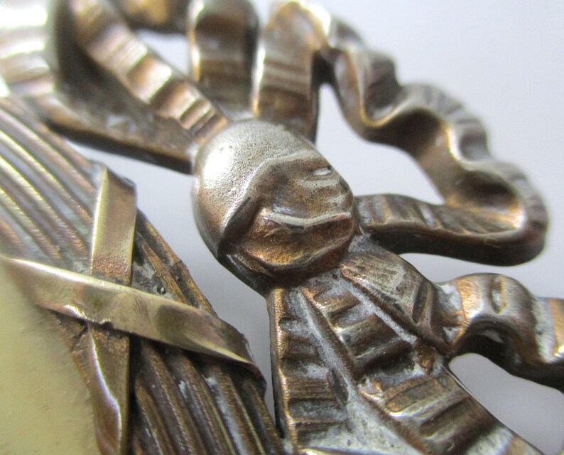 May include: A close-up of a decorative metal ornament featuring a stylized bow with intricate details. The ornament is made of brass and has a worn, antique finish.