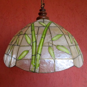 Può includere: Una lampada a sospensione bianca e verde con un design a bambù. La lampada è realizzata in madreperla e ha una parte superiore in legno.