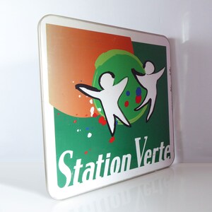May include: A green and orange sign with the text "Station Verte" in white. Two white figures are dancing on the sign, with a green circle behind them. The figures are outlined in black.