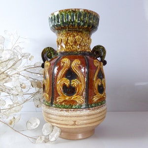 Puede incluir: Un jarrón de cerámica marrón y verde con intrincados diseños florales. El jarrón tiene una boca ancha y dos asas.