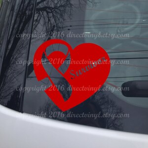 Può includere: Adesivo in vinile rosso a forma di cuore con un nastro rosso e la parola "Survivor" all'interno. L'adesivo è sul lunotto posteriore di un'auto.