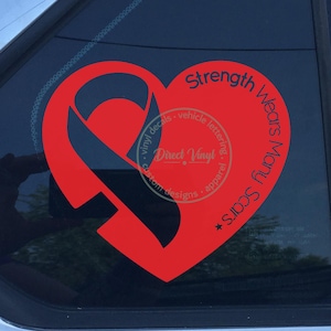 Peut inclure: Un autocollant en vinyle rouge appliqué sur une vitre de voiture en forme de cœur avec un ruban de sensibilisation intégré. Le texte "Strength Wears Many Scars" est imprimé le long du côté droit du cœur dans une police sans empattement.