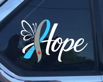 Puede incluir: Un adhesivo de vinilo blanco, azul claro y gris aplicado en la ventana de un coche. El diseño presenta un ala de mariposa unida a un lazo de concienciación, con la palabra Hope en letra cursiva blanca y un pequeño icono de gota roja.