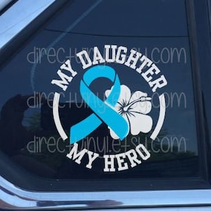 May include: A white vinyl decal with the text "My Daughter My Hero" in a circle. A blue ribbon with a white flower is in the center of the circle.