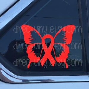 Può includere: Un adesivo a forma di farfalla arancione brillante con un motivo a nastro, applicato al finestrino di un'auto. L'adesivo presenta il testo "directvinyl.etsy.com". Le ali della farfalla sono dettagliate e il nastro è centrato nel design.