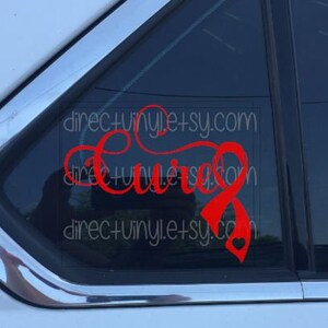 Può includere: Decalcomania in vinile rosso con la parola "Cure" e un nastro rosso con un cuore al centro. La decalcomania è su un finestrino di un'auto.